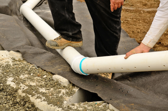 The man stepping on the white pipe and the other man helding the pipe for French drain kitchener, ON